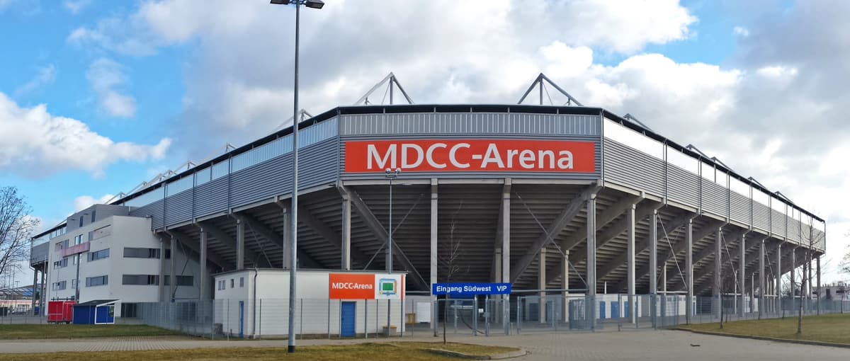 Außenansicht des Magdeburger Stadions mit dem Schriftzug MDCC-Arena an der Fassade und offenem Tribünenunterbau.