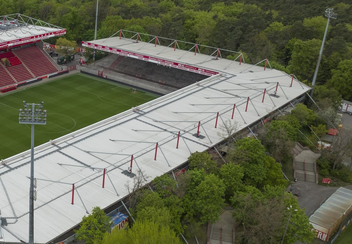 Luftaufnahme der überdachten Stehplatztribünen des Stadions An der Alten Försterei, umgeben von Bäumen.