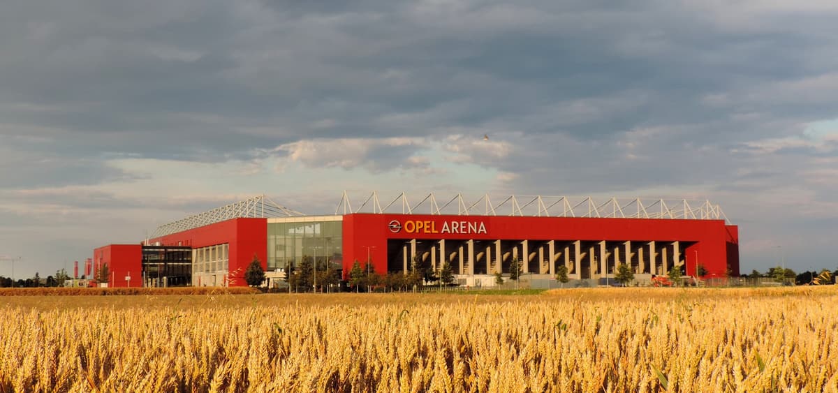 Die rote Fassade der Mainzer Arena mit dem damaligen Schriftzug Opel Arena hinter einem Getreidefeld.