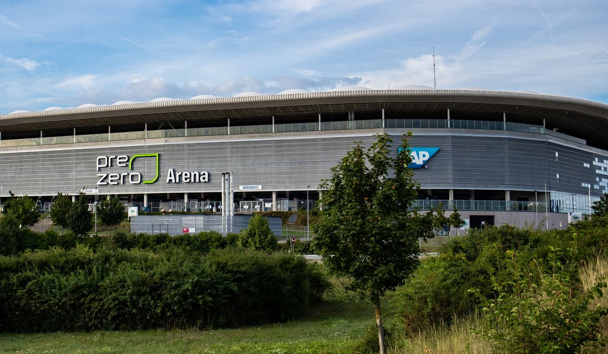 Außenansicht der Arena in Sinsheim mit der Fassade und dem Schriftzug „PreZero Arena“, im Vordergrund Büsche und ein junger Baum.