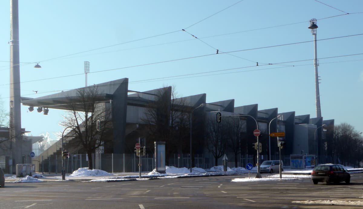 Außenansicht des Städtischen Stadions an der Grünwalder Straße von Osten mit den gezackten Dachelementen der Tribüne und Flutlichtmasten an einem Wintertag.
